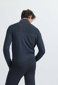 Suéter azul marino con una sección de punto texturizado en la parte superior de la espalda y una sección inferior lisa; cuenta con una cinturilla ribeteada y acentos en el cuello.