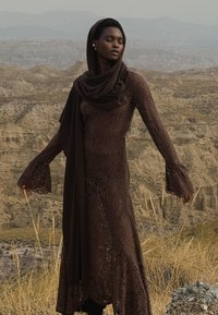 Hnedé čipkované šaty s dlhými rukávmi a rozšírenými manžetami, doplnené zladeným šálom. Vzor obsahuje kvetinové motívy a vyrezávané detaily.