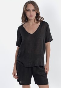 Top in lino nero con scollatura a V e maniche corte arrotolate, abbinato a pantaloni corti in lino nero. Tessuto morbido e vestibilità comoda.
