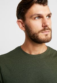 T-shirt din bumbac de culoare verde măslin cu guler rotund. Textură moale, mâneci scurte și un design simplu, fără modele sau embellishments.