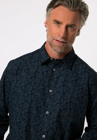 Námořnická košile s knoflíky, zdobená vzorem listů, vyrobená z hladkého materiálu s jemnou texturou. Obsahuje klasický límec a světlé knoflíky.