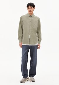 Lichtgroen overhemd met lange mouwen en knopen, voorzien van een zak, gecombineerd met donkerblauwe broek met losse pasvorm en grijze sneakers met witte accenten.
