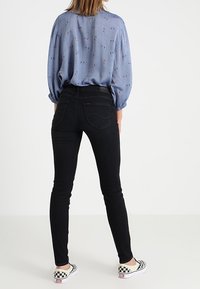 Jeans oscuros ajustados combinados con una blusa de estampado azul claro. El conjunto incluye zapatos sin cordones de cuadros y presenta una textura de tela suave.