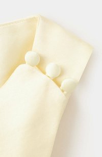 Gros plan d'un poignet en tissu jaune pâle avec trois boutons ronds recouverts de tissu en ligne.