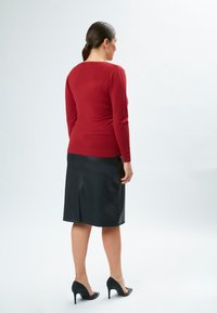 Roter Pullover mit langen Ärmeln, kombiniert mit einem schwarzen Lederrock in Kniehöhe, der mit einem Schlitz hinten versehen ist und mit schwarzen High Heels getragen wird.