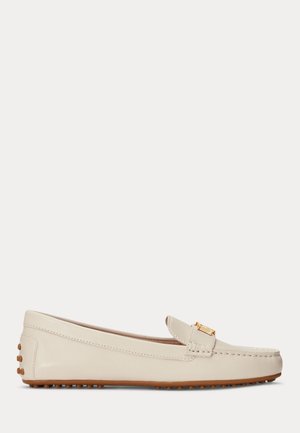 Beige leren loafer met een afgeronde neus, gouden gesp op de band en rubberen noppenzool voor grip en comfort.