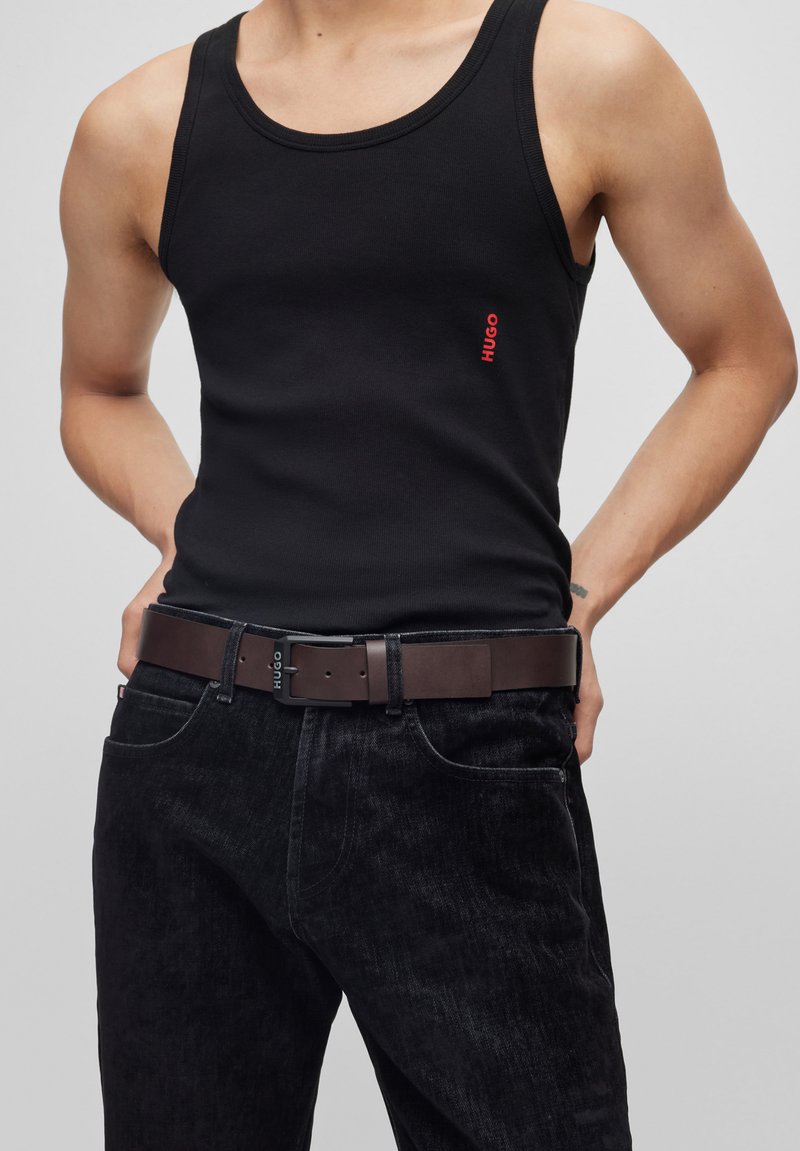 Un débardeur en coton noir avec un logo rouge discret "HUGO". Associe à un jean en denim foncé et une ceinture en cuir marron avec une boucle de marque.
