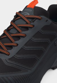 Μαύρο και γκρι αθλητικό παπούτσι με κορδόνια με πορτοκαλί ρίγες και πορτοκαλί θηλιά έλξης στη γλώσσα, με υφή και σχέδιο στην πλευρά.