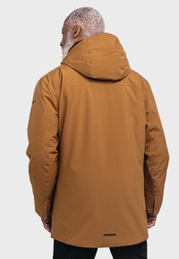 Braune Kapuzenjacke mit glatter Textur, die eine taillierte Passform und ein minimalistisches Design aufweist. Enthält einen schwarzen Akzent am Saum.