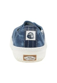 Baskets en toile bleu denim avec semelle blanche, présentant un patch logo de lion et un design à rayures verticales au niveau du talon. Logo "VANS OFF THE WALL" affiché.