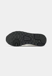 Black rubber sole with circular and ridged patterns, featuring a raised logo and a slight heel. Material appears durable and textured.