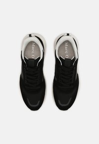 Baskets athlétiques noires présentant une combinaison de matériaux lisses et texturés, bout rond, semelle rembourrée et accents blancs contrastants.