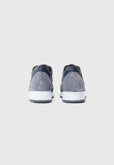 Hall gray suede spordijalatsid valgete talladega, nähtuna tagantpoolt, heledal hallil taustal.
