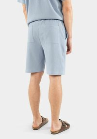 Ljusblå randiga shorts, elastisk midja, två bakfickor och en avkopplad passform. Bärs med bruna sandaler. Slät textur.