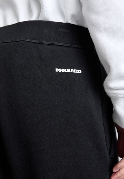 Black sweatpants featuring a smooth texture and elastic waistband. White "DSQUARED2" logo printed on the upper thigh area.