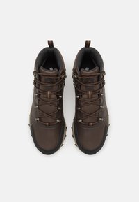 Botas de senderismo marrones con una parte superior de malla texturizada, puntera reforzada y suela de goma flexible. Presenta un cordón intrincado y una lengüeta.