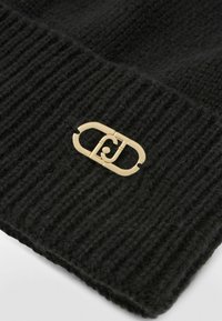 Czarna, prążkowana czapka beanie z detalem w postaci złotego logo. Materiał wydaje się miękki i teksturowany, co wzbogaca ogólny design.