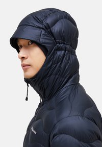 Navy puffer jacket with quilted texture, high collar, and integrated hood. Features a front zipper and adjustable drawstrings at the neck.