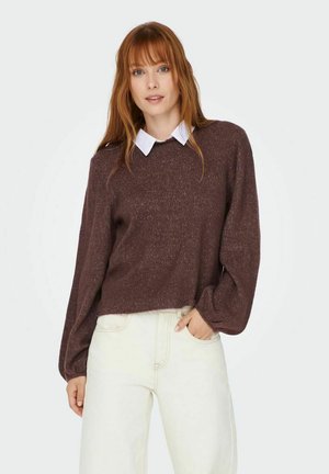 Pull en tricot texturé marron avec un col rond et des manches longues légèrement bouffantes, superposé sur une chemise blanche à col.