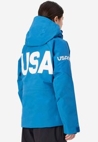 Giacca impermeabile blu con cappuccio, caratterizzata da un grande logo bianco "USA" sul retro e accentuazioni sottili sulle maniche.