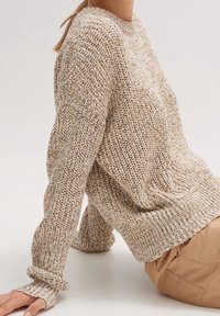 Sweter dzianinowy w beżowym i kremowym kolorze, o luźnym kroju, z prążkowanymi mankietami i textured materiałem. Posiada okrągły dekolt i opuszczone ramiona.