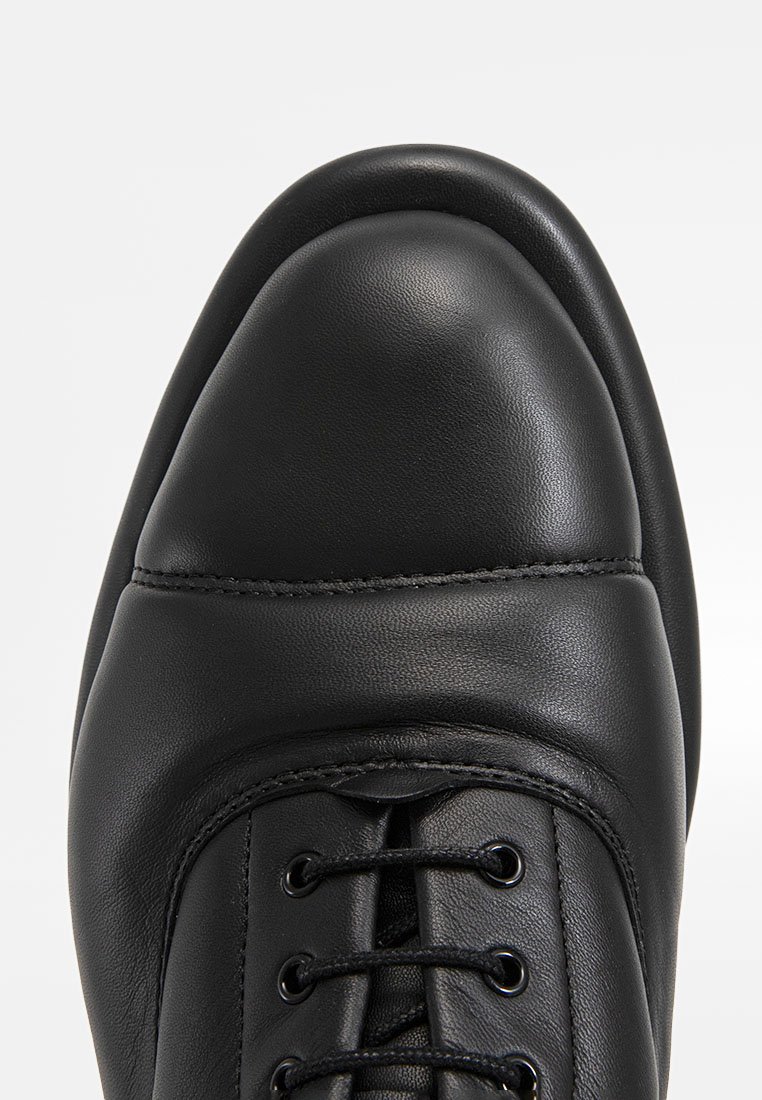 Chaussure en cuir noir avec un bout arrondi, un laçage à l'avant, une texture lisse et un design minimaliste avec de subtils détails de couture.