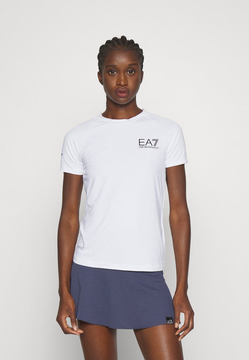Witte korte mouw atletische shirt met EA7-logo op de linker borst. De stof lijkt lichtgewicht en ademend. Gecombineerd met een marineblauwe geprinte rok.