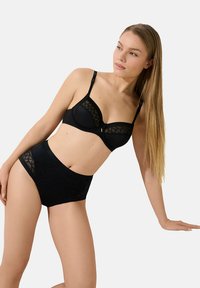 Ensemble noir de soutien-gorge et culottes taille haute avec superposition de dentelle à motifs géométriques, bretelles réglables et texture de tissu lisse.