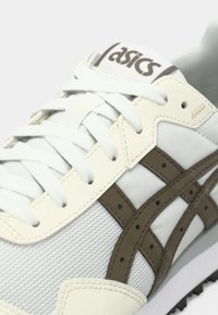 Valged jooksujalanõud, millel on tekstuuriga võrkkangas, pruuni nahaga detailid ja traditsiooniline paelakinnitus, millel on nähtavad õmblusdetailid.