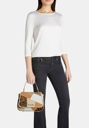 Mujer con camiseta blanca de manga larga y vaqueros negros sostiene un pequeño bolso patchwork con estampado de leopardo y paneles en color tostado, beige y blanco.