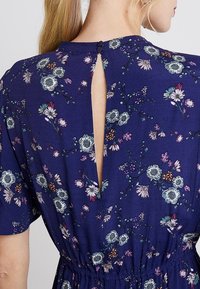 Blommig klänning i marinblått tyg med korta ärmar, en insvängd midja och en nyckelhålsdetalj i ryggen med två knappar.