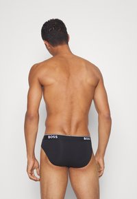 Boxers noirs avec une ceinture élastique brandée, présentant une texture lisse et un design ajusté. Logo visible sur la ceinture.