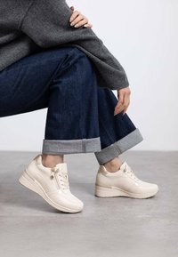 Zapatillas beige con acabado de cuero suave, diseño con cordones y detalle de cremallera decorativa. Suela gruesa y elevada con un ligero brillo.