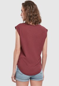 Burgunderfarget ermeløs t-skjorte med avrundet kant, som har en avslappet passform og myk tekstur, kombinert med lyseblå denimshorts.