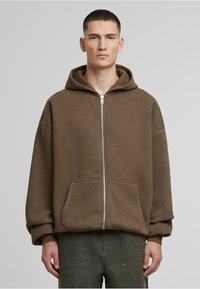 Brauner Reißverschluss-Hoodie mit großer Kapuze, Fronttaschen und gerippten Ärmeln, aus weichem Material, lockere Passform, minimales Design.