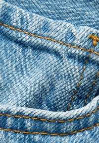 Tela de mezclilla azul con un tejido texturizado, que presenta costuras y pliegues en amarillo contrastante. Vista en primer plano de los detalles del material.