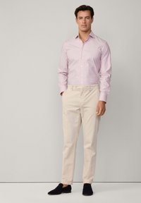 Camicia a righe rosa chiaro e bianca con bottoni, abbinata a pantaloni beige e mocassini neri, che mette in risalto una vestibilità sartoriale e linee pulite.