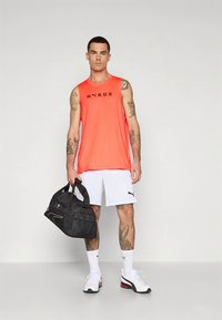 Sportoutfit med en ljus orange ärmlös topp med svart text, vita shorts och svart sportväska. Vita sneakers med detaljer.