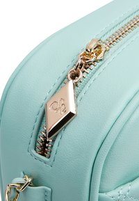 Una borsa in ecopelle turchese con una zip dorata e un tirante a forma di diamante, con dettagli cuciti lungo i bordi.