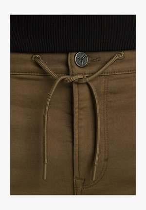 Smeđe hlače s zatvaranjem na vezicu, metalnim dugmetom i šivenim detaljima. Tekstura je glatka, s jednoličnom bojom i bez uzoraka.