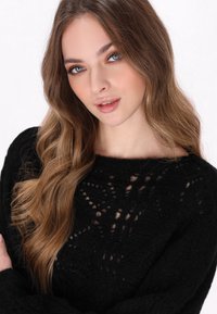 Schwarzer gestrickter Pullover mit weiter Ausschnittöffnung, der filigrane, spitzenartige Muster und eine weiche, strukturierte Oberfläche aufweist.