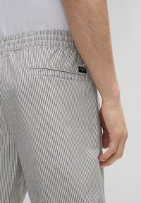 Gestreifte Shorts in einem hellgrauen und marineblauen Muster, gefertigt aus atmungsaktivem Stoff. Mit einem elastischen Bund und einer Gesäßtasche mit Branding.
