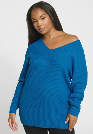 Maglione blu lavorato a maglia con scollo a V ampio, spalle cadenti e maniche lunghe; texture a costine in tutta la sua lunghezza e vestibilità leggermente oversize.