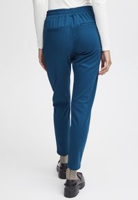 Tyrkysové elastické kalhoty se zapínáním na gumu, dvěma zadními kapsami a Slim fit. K tomu jsou doladěny tmavými platformovými botami a vzorovanými ponožkami.