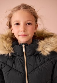 Černá prošívaná bunda s texturovaným povrchem a kapucí lemovanou kožešinou, se zlatým zipem a diagonálními stehy.