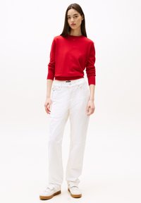 Maglione rosso a maniche lunghe abbinato a pantaloni bianchi a gamba larga e sneakers bianchi. Design semplice senza motivi o accenti visibili.