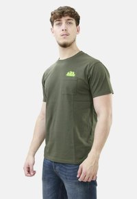 T-shirt in cotone verde oliva con scollo rotondo, maniche corte e taschino sul petto con un design grafico verde brillante.