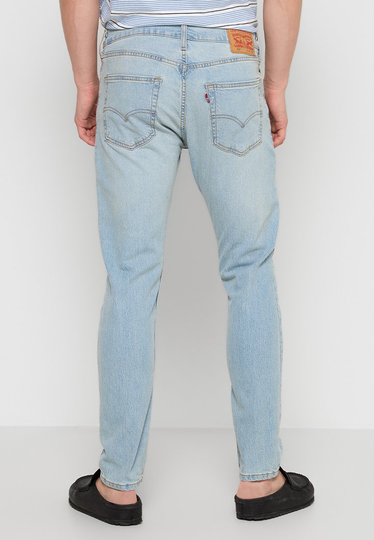 Jean en denim bleu clair avec une coupe slim, présentant une étiquette logo à l'arrière, deux poches arrière et des accents de couture.