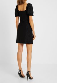 Svart miniklänning med puffärmar och fyrkantig halsringning. Texturerad tyg med diamantmönster. Bärs med svarta högklackade sandaler.