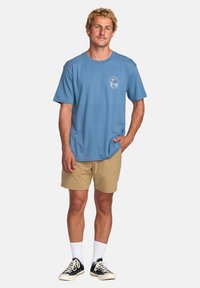 Blå bomull T-skjorte med korte ermer, brystlogo trykk, kombinert med beige shorts og svarte sneakers, med hvite sokker.